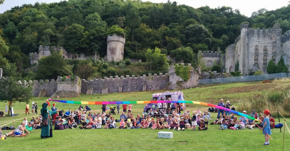 A crowd watching a magician perform at Gwrych Castle; a long rainbow streamer is held between the magician and a child, billowing in the wind