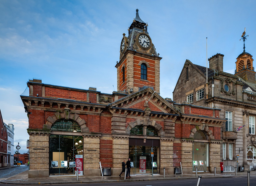 The exterior of Crewe Market Hall. An old building with red and yellow bricks, there is a central clock tower.