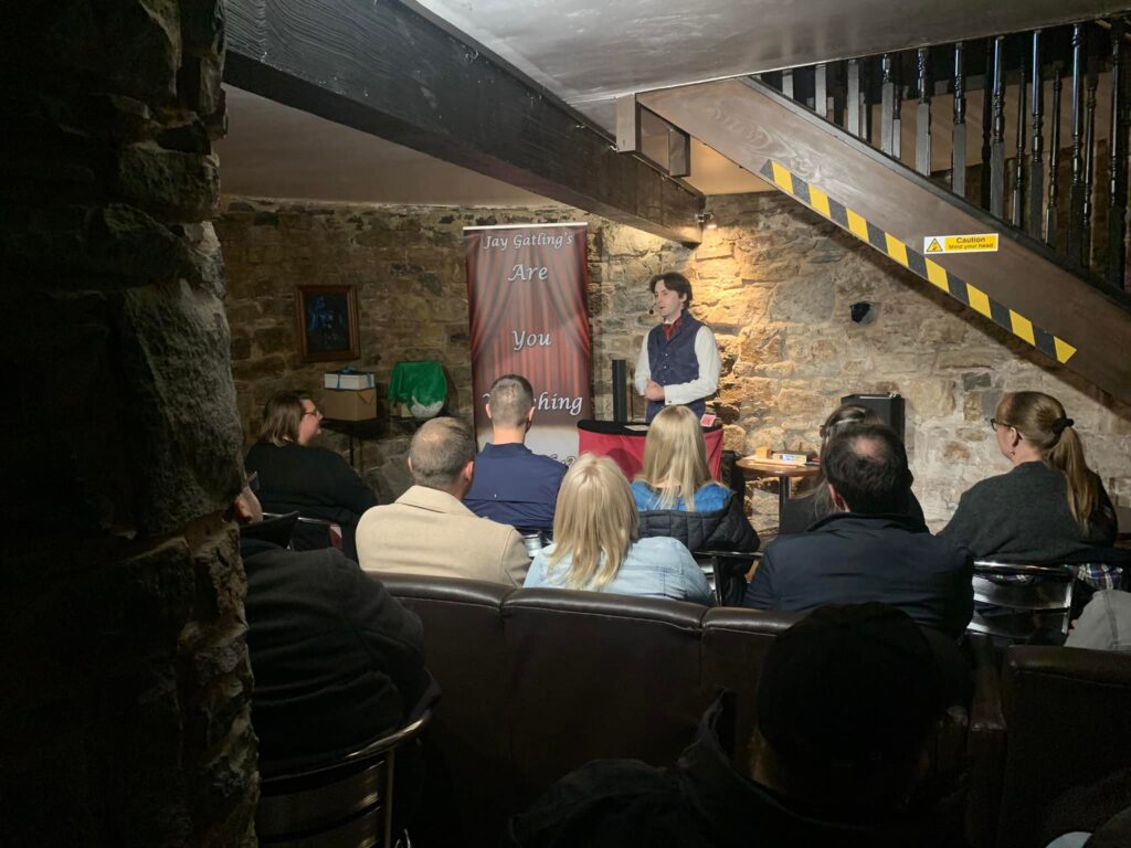 Magician Jay Gatling in front of an audience. He is in a small circular room with thick stone walls, at the base of a medieval tower.