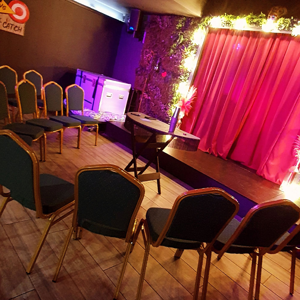 A semi-circle of chairs surrounding a small table. A red stage curtain is in the background.